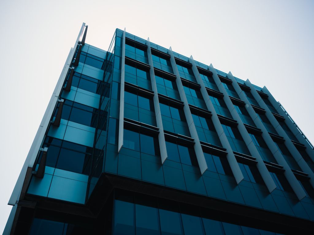 Low angle view of a modern office building with glass facade and geometric design in an urban setting.